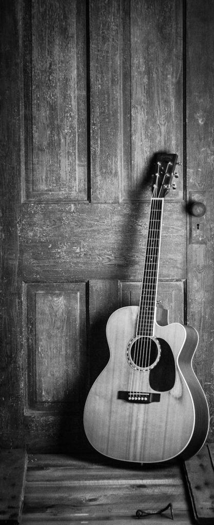 A classic acoustic guitar leaning against a rustic wooden door in a black and white vintage style.