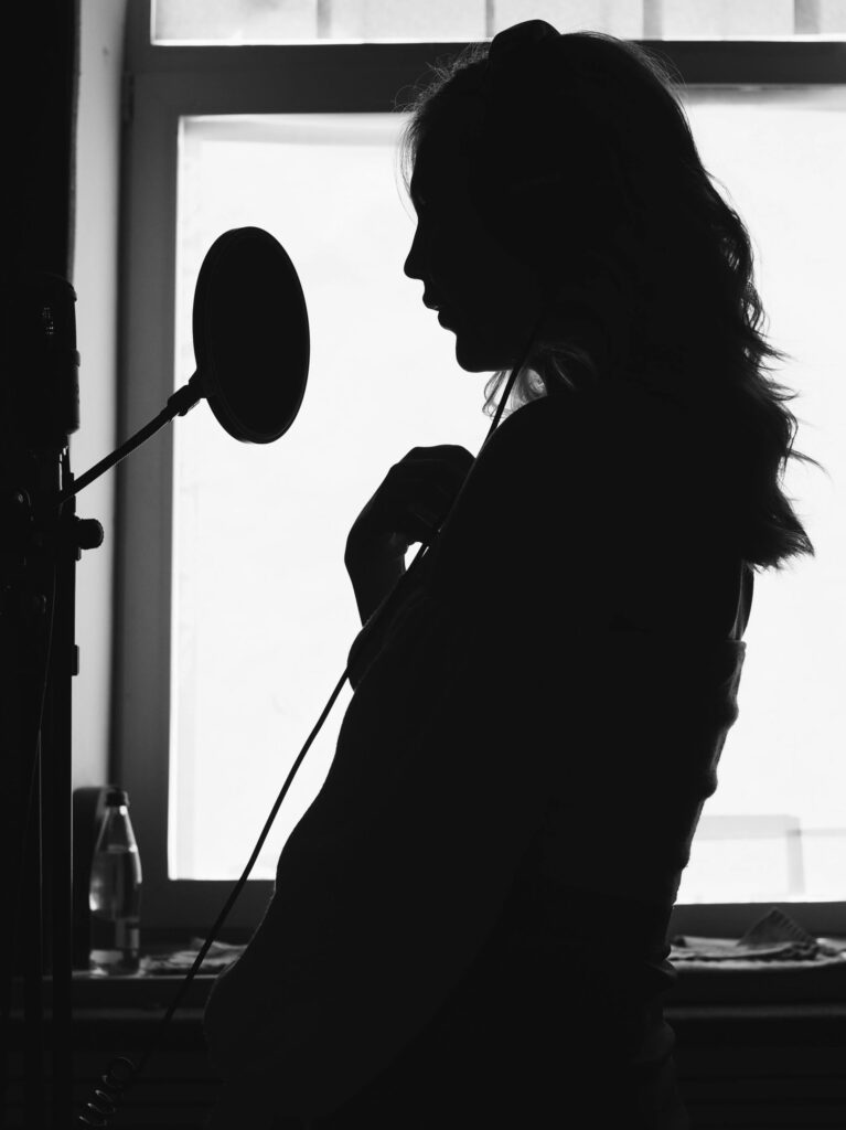 A dramatic silhouette of a woman singing into a microphone in a recording studio.